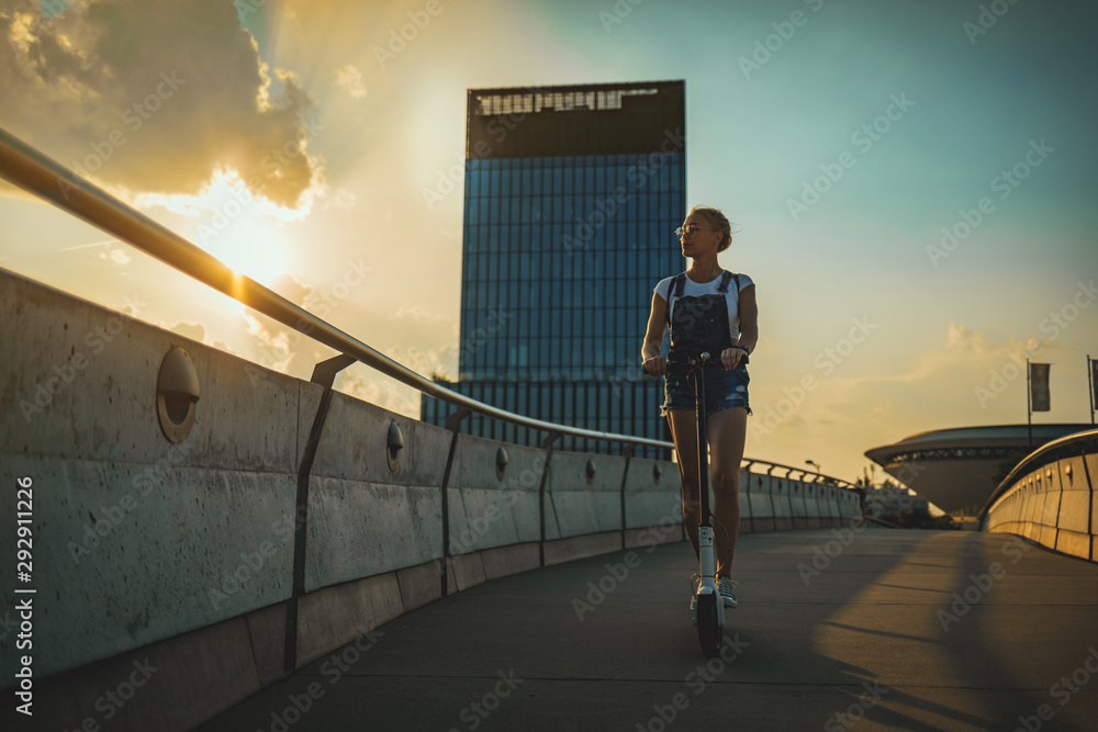 现代城市建筑背景下骑着电动滑板车的女人