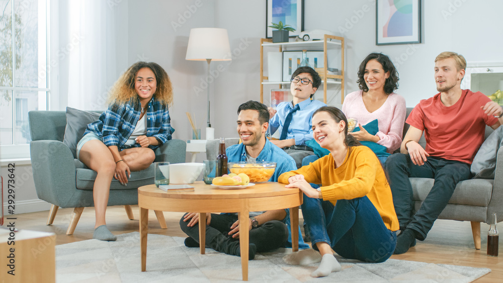 At Home Diverse Group Friends Watching TV Together, Eating Snacks and Drinking Beverage. They Probab