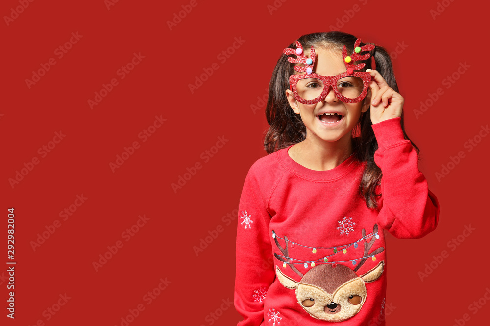 Cute girl in Christmas sweater and party glasses on color background