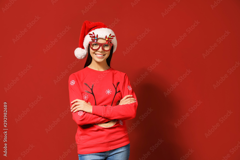 Funny woman in Christmas sweater and Santa hat on color background