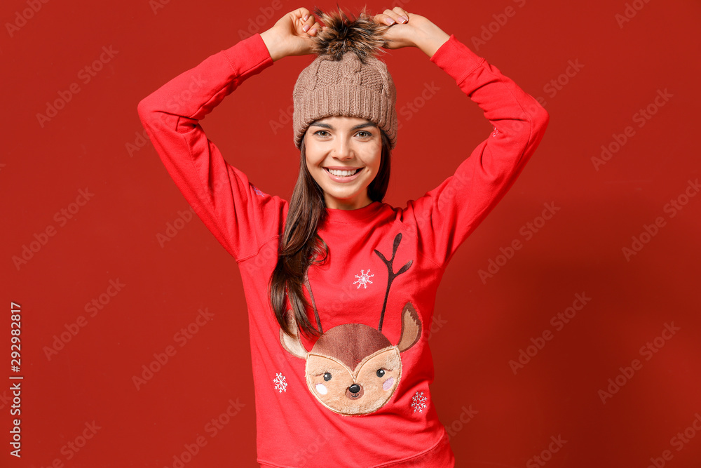 Young woman in Christmas sweater and knitted hat on color background