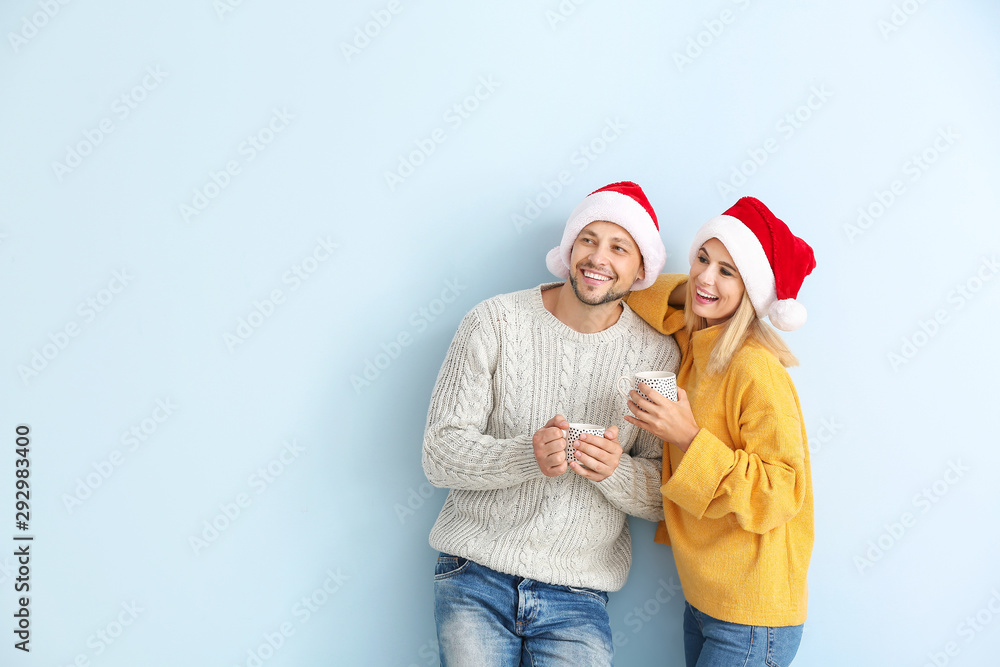 Happy couple in Santa hats drinking hot chocolate on color background