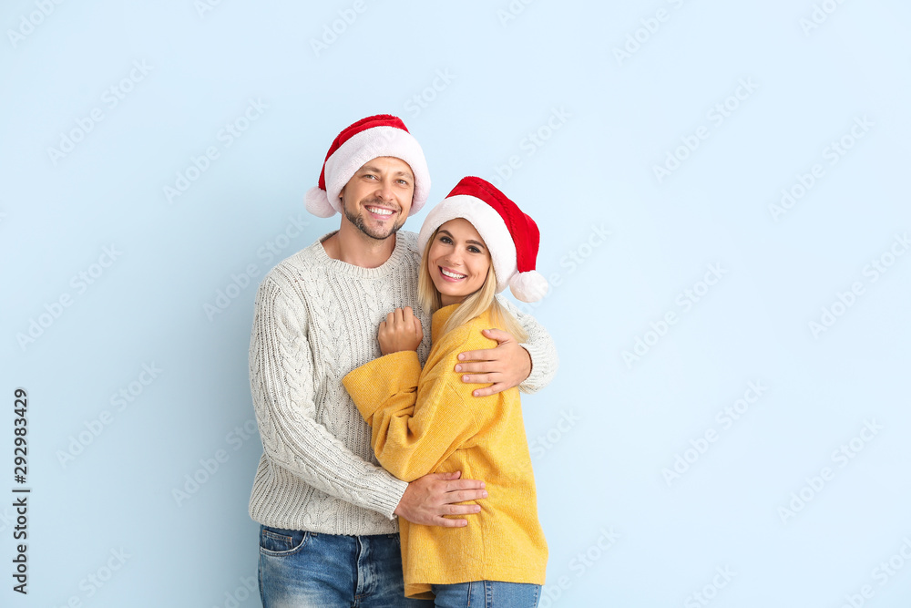 Happy couple in Santa hats on color background