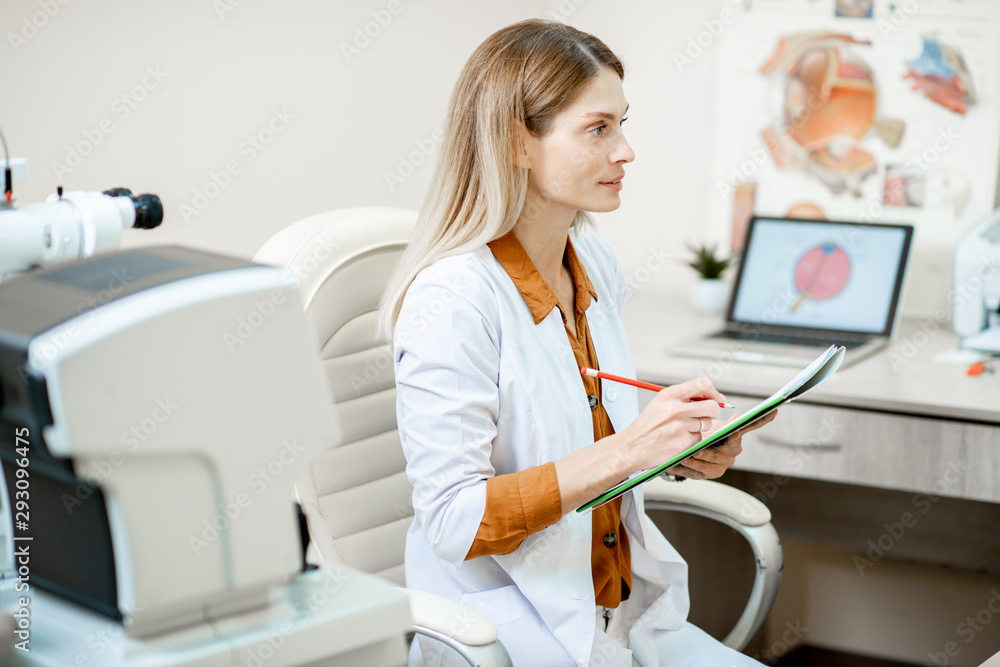 Beautiful female ophthalmologist writing a medical recipe or patients history while sitting in opht