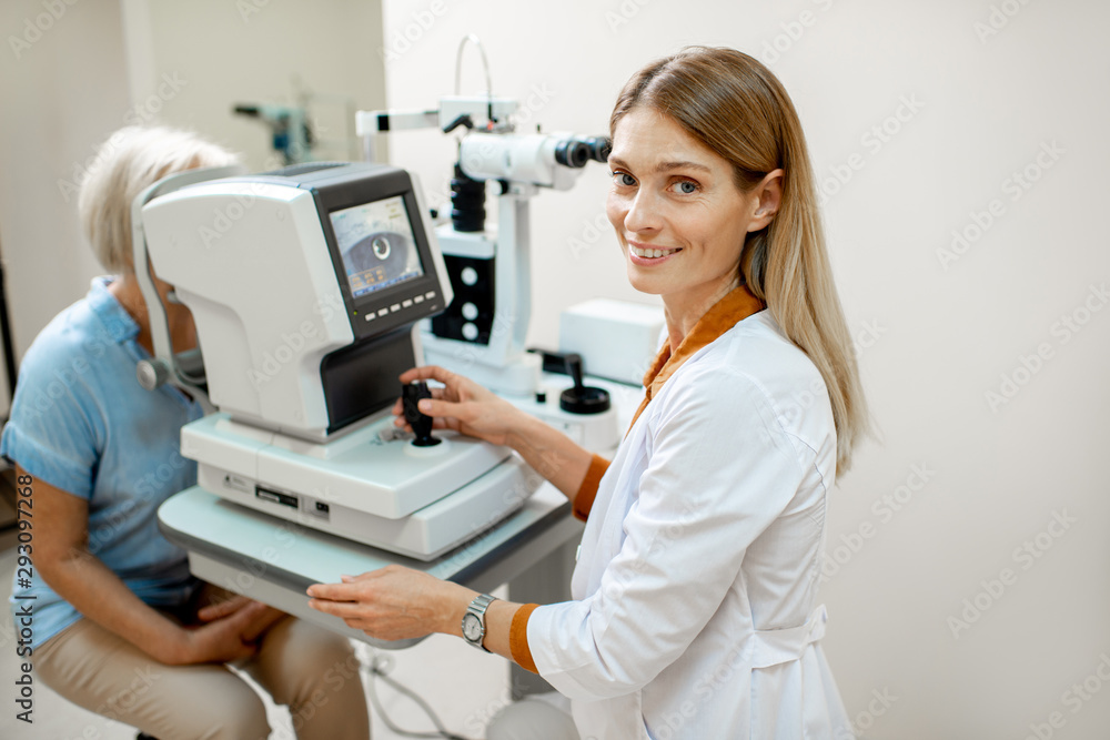 Portrait of a female ophthalmologist examining eyes of a senior patient using digital microscope dur