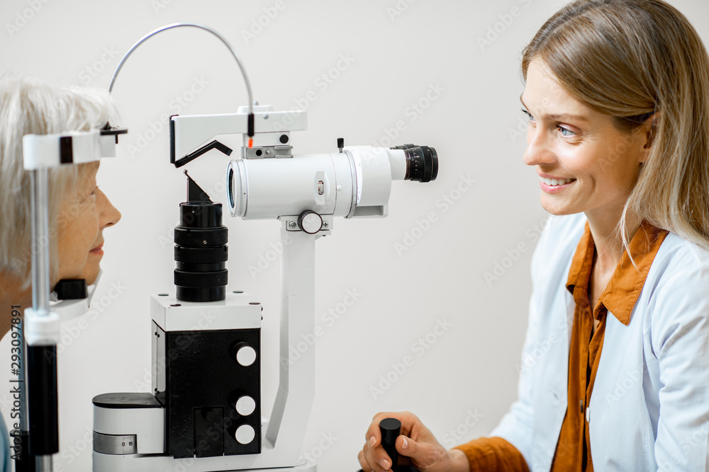 Cheerful ophthalmologist examining eyes of a senior patient using microscope during a medical examin