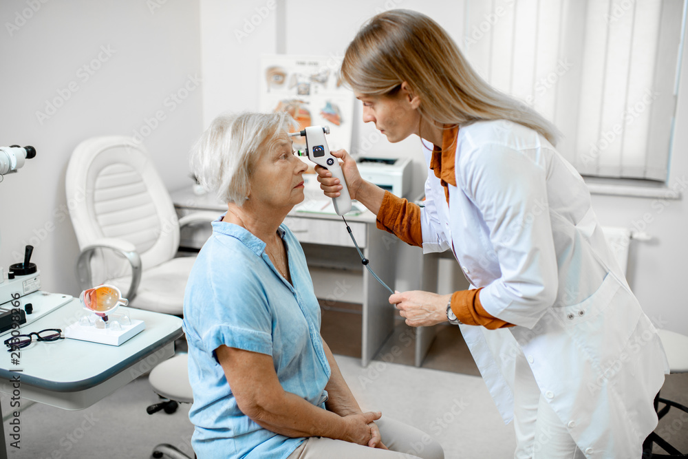 Female ophthalmologist measuring the eye pressure with modern tonometer to a senior patient in the m