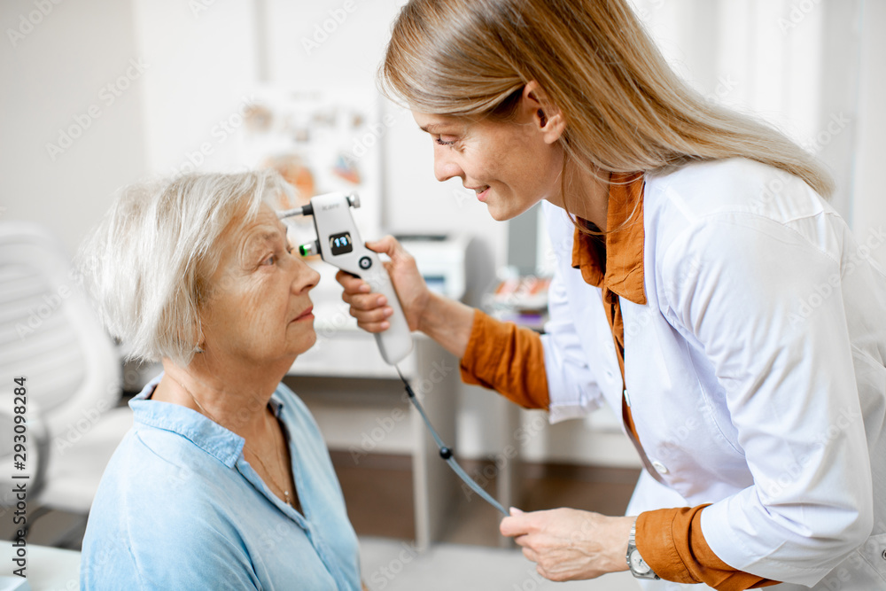 Female ophthalmologist measuring the eye pressure with modern tonometer to a senior patient in the m