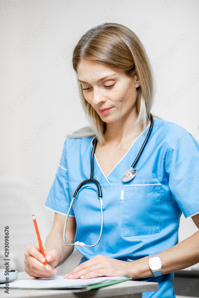 Portrait of a beautiful nurse in blue uniform with stethoscope writing medical history or recipe in 