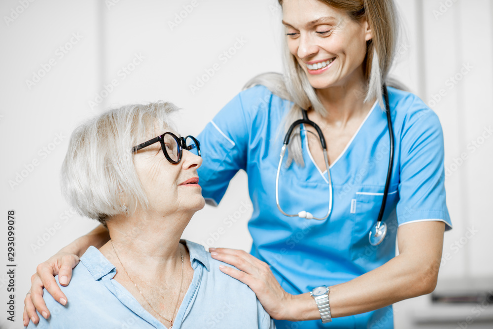 Nurse taking care of senior woman, hugging her shoulders in the clinic or home for elderly