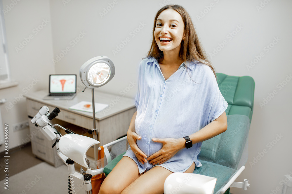 Smiling pregnant woman sitting on the gynecological chair before a medical examination by a gynecolo