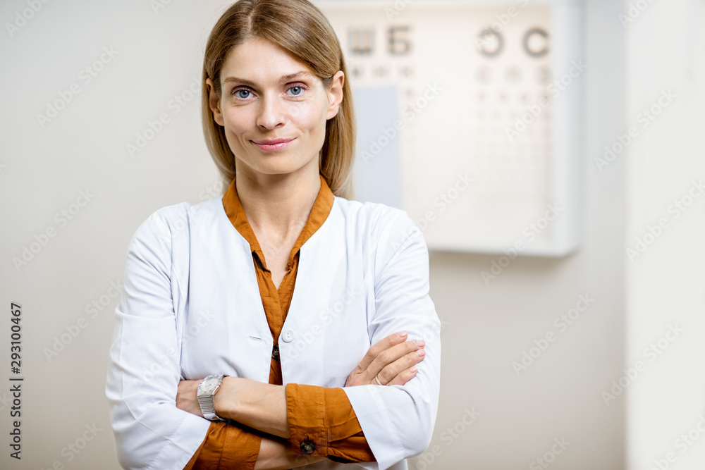 Portrait of a confident ophthalmologist in medical uniform standing in front of eye chart in the oph