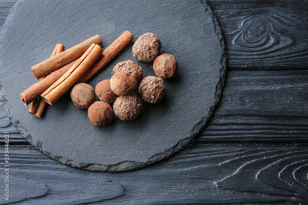 Slate plate with tasty sweet truffles and cinnamon on dark table