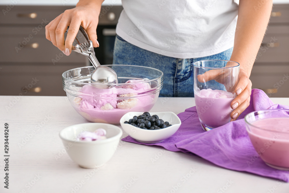 Woman putting tasty blueberry ice cream into glass in kitchen