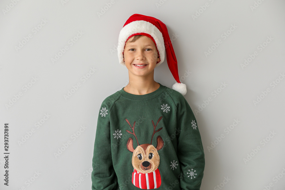 Funny boy in Christmas sweater and Santa hat on light background