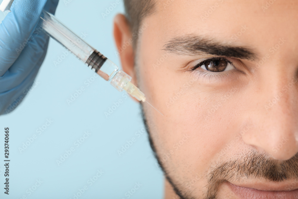 Handsome man receiving filler injection on color background, closeup