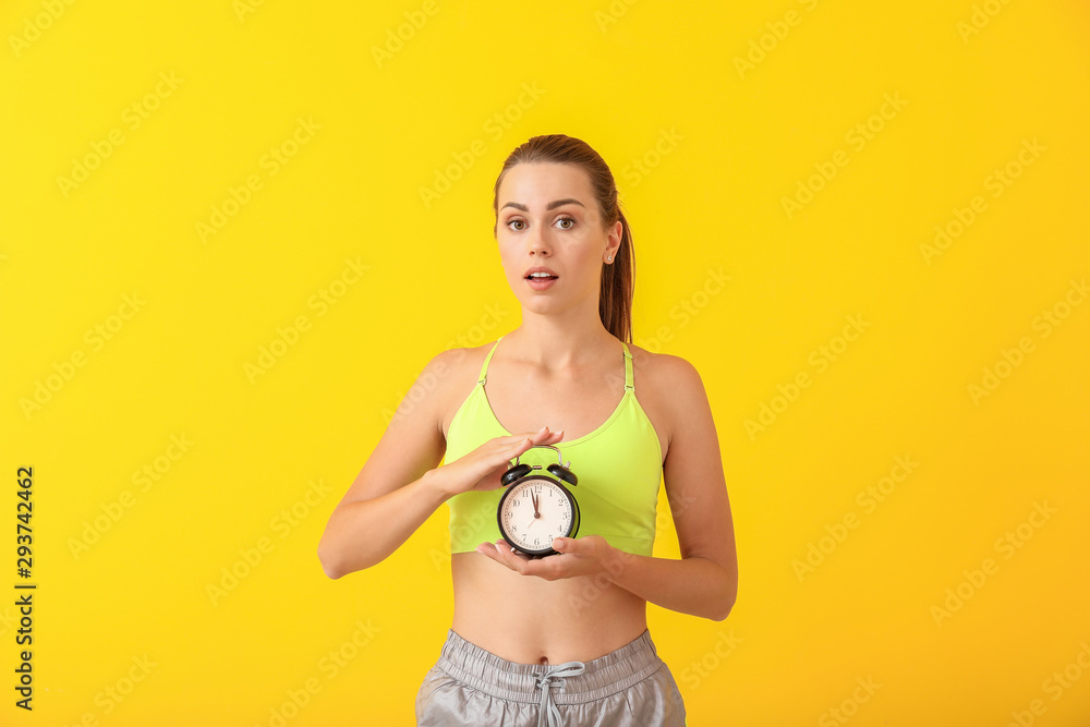 Worried young woman with alarm clock on color background