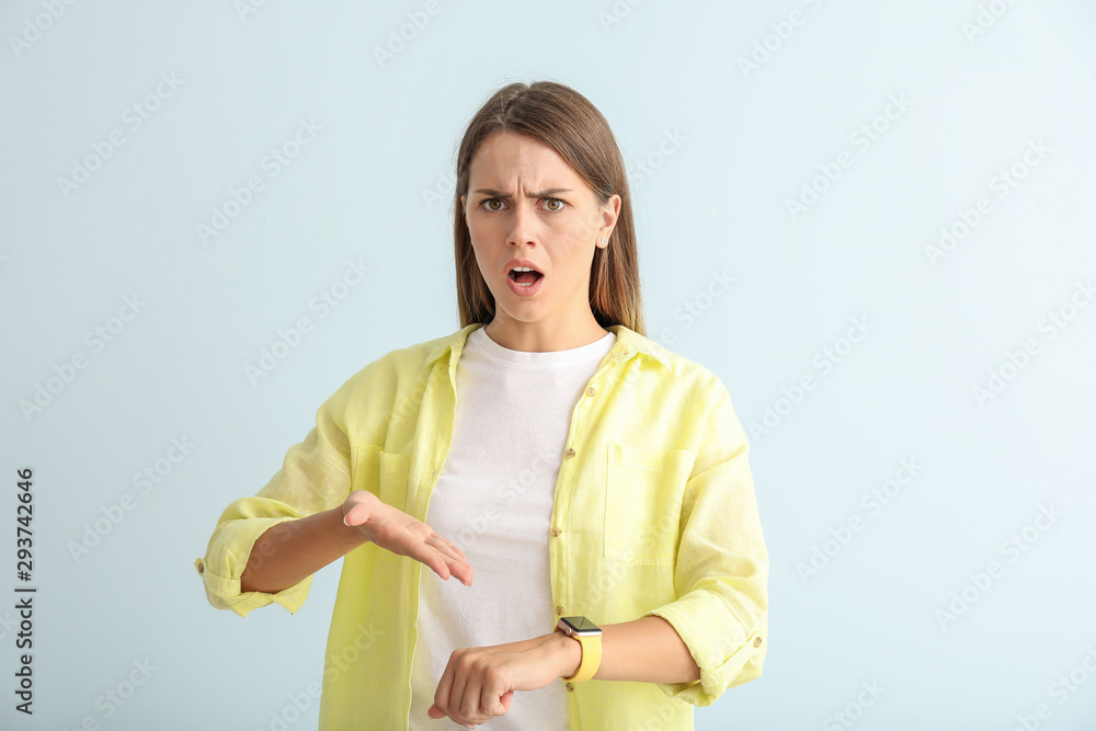 Angry young woman with watch on color background