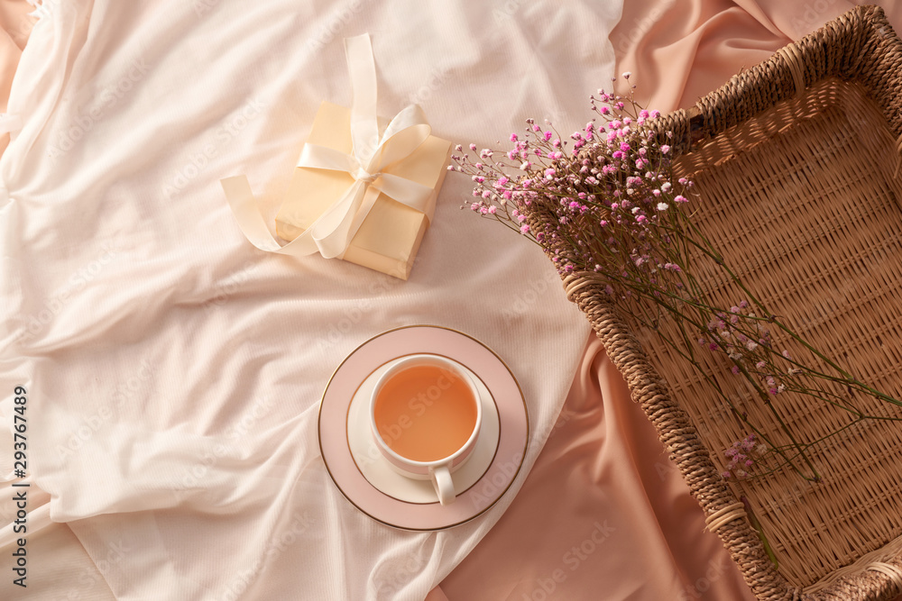 Cup of tea, gift box and flowers on tray on light fabric background