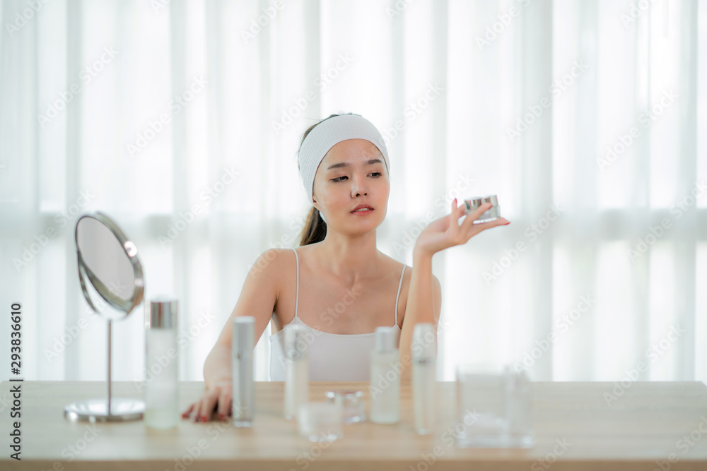 Portrait of Charming Asian woman having jar with face cream in hand, using, applying lotion, enjoyin