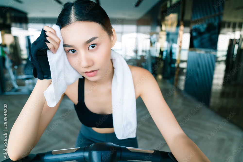 strong and firm asian woman sport wear relax on bicycle hand hold white napkin fitness background