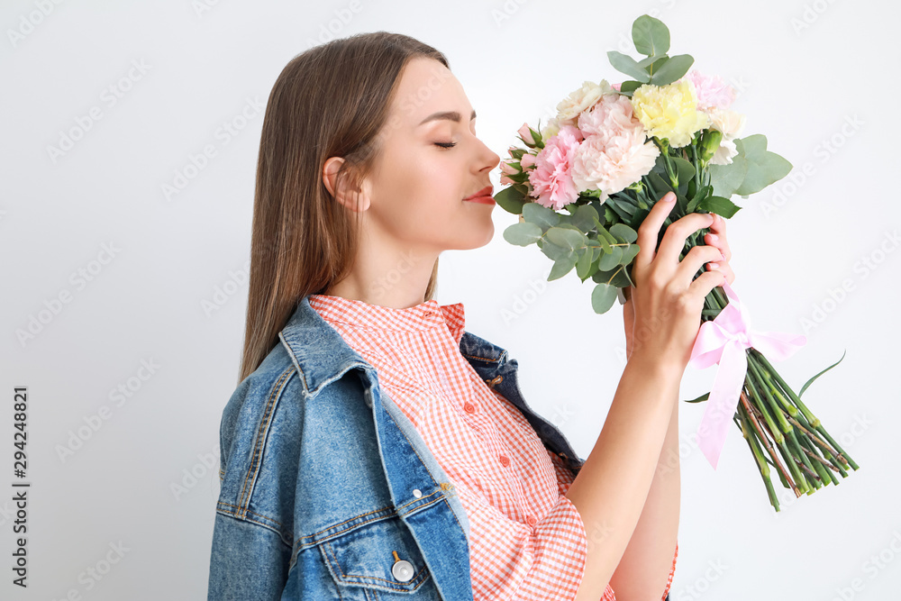 Beautiful young woman with bouquet of carnation flowers on light background