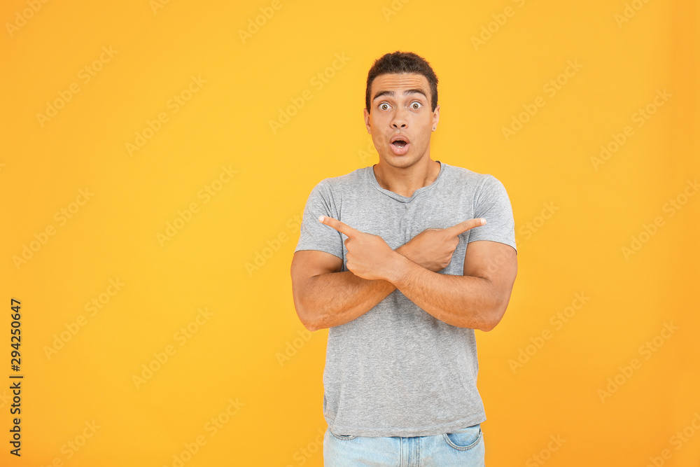 Surprised African-American man pointing in different directions on color background