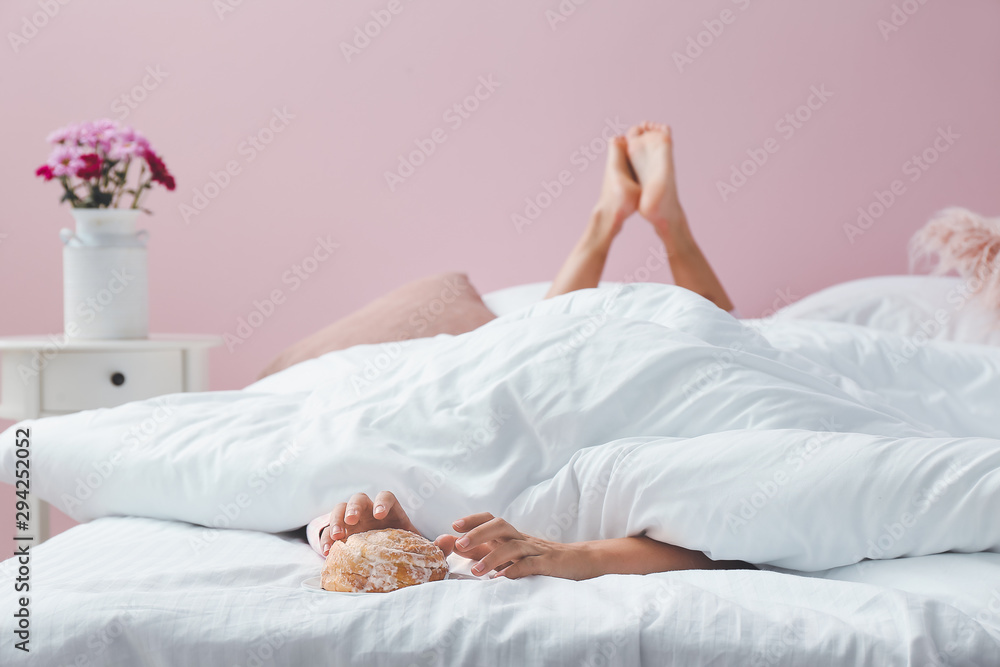 Young woman reaching hands for tasty bun while lying in bed