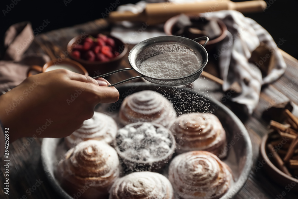 Woman sprinkling sugar powder onto buns, closeup