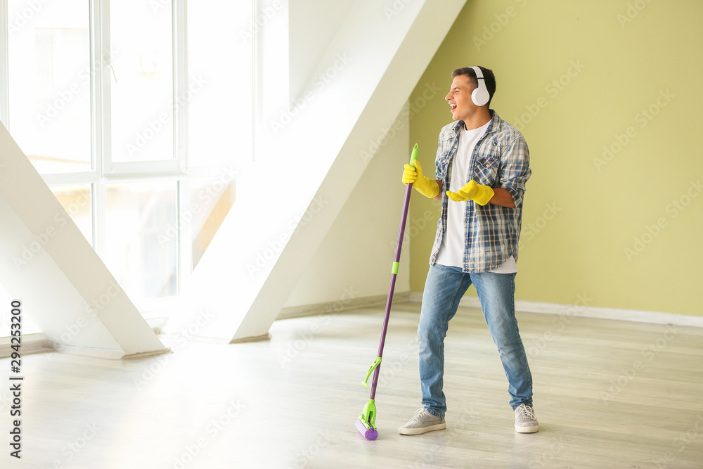 Young man listening to music and singing while cleaning his flat