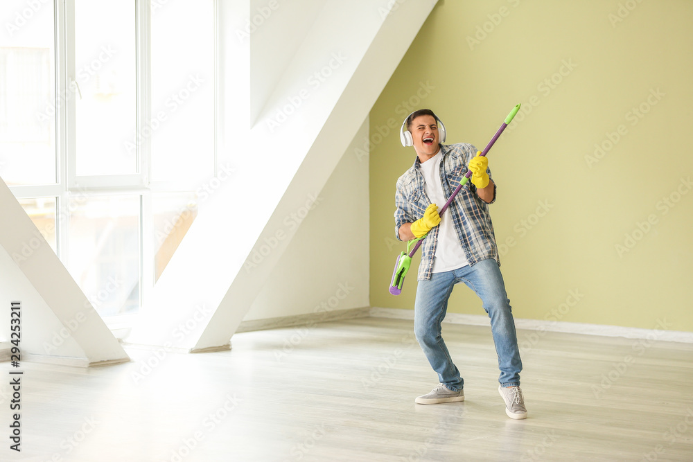 Young man listening to music and singing while cleaning his flat