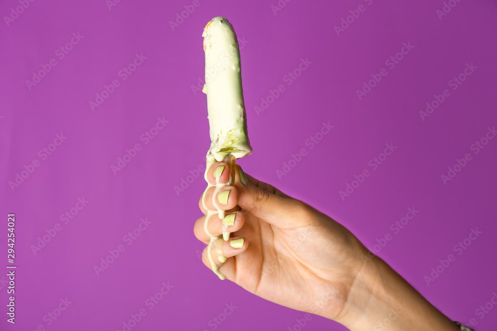 Female hand with tasty pistachio ice cream on color background