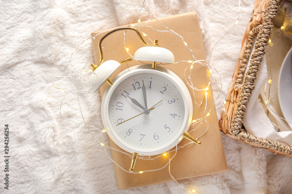 Alarm clock with book and glowing garland on plaid