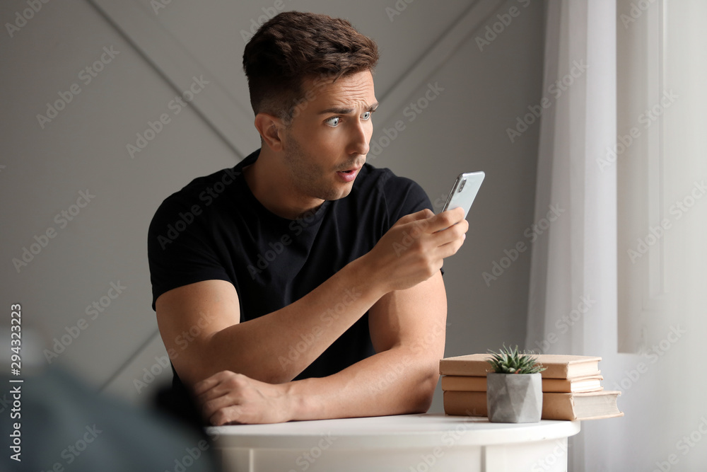 Shocked young man with mobile phone at home