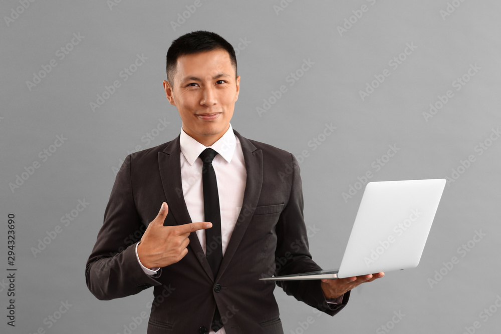 Asian businessman with laptop on grey background