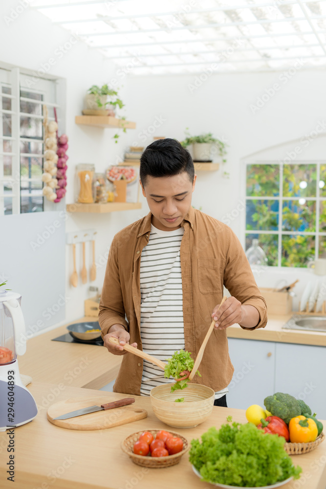 微笑的年轻人在家的厨房里做蔬菜沙拉