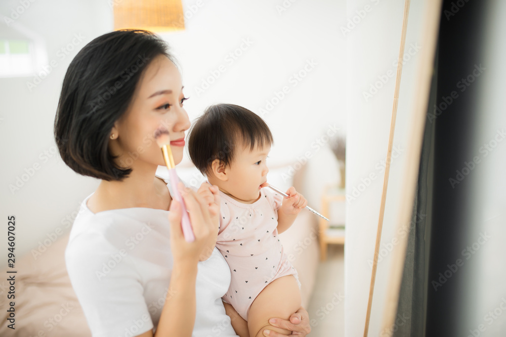 家里有个有趣的家庭。妈妈和她的小女儿正在化妆，在镜子附近玩得很开心。巴