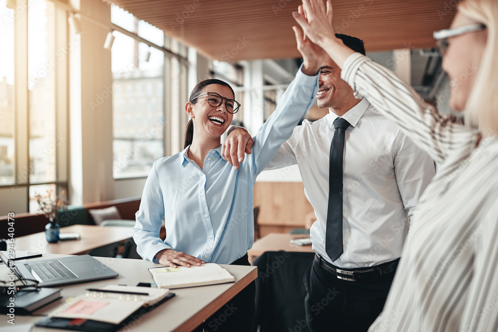 Laughing businesspeople high fiving together in an office