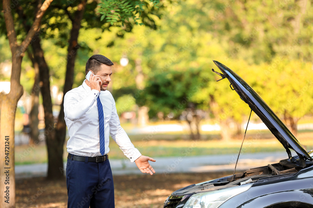 Businessman talking by phone near broken car outdoors