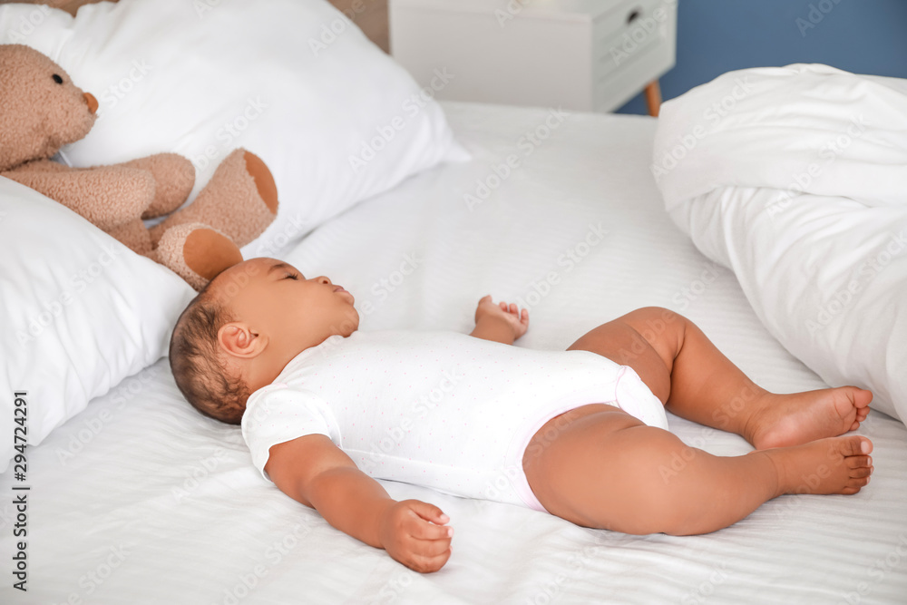 Cute African-American baby sleeping on bed