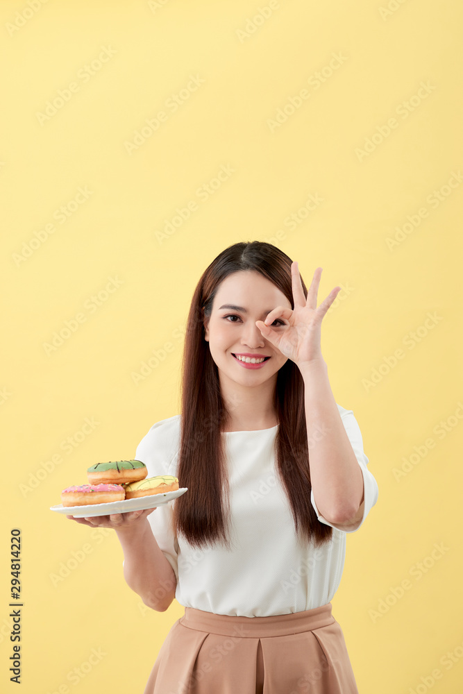 拿着盘子甜甜圈的年轻女子用手指做ok手势，这是一个极好的象征