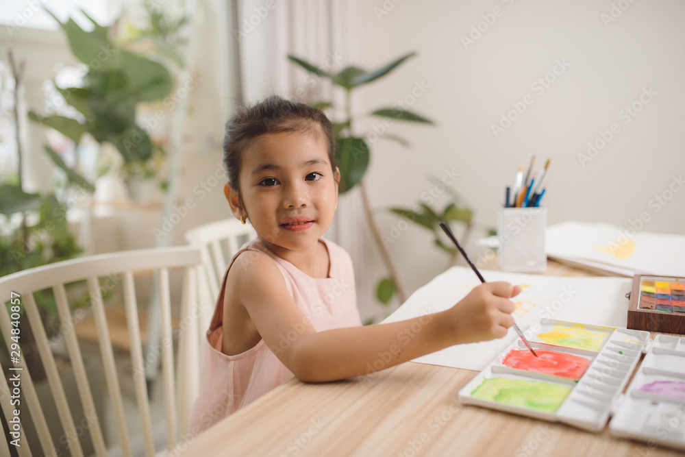 可爱的亚洲小女孩在家里用纸、水彩和画笔画画。