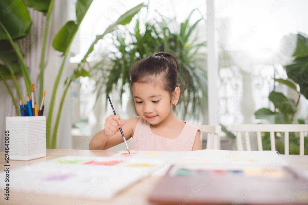 可爱的亚洲小女孩在家里用纸、水彩和画笔画画。