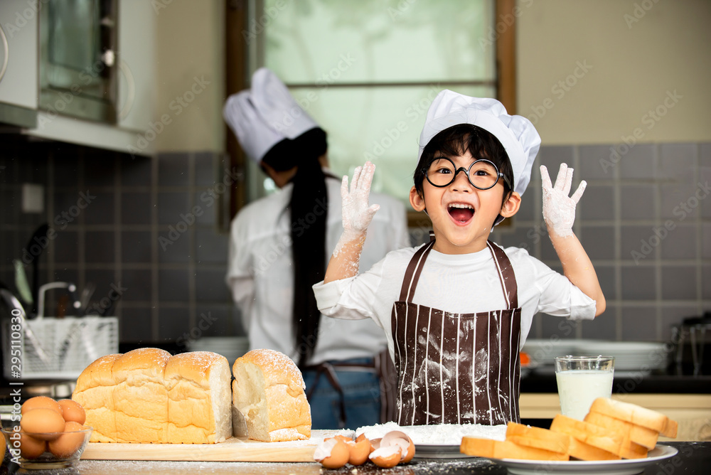 Cute little asian boy a in chef  hats smiling while preparing for baking the dough  in kitchen room 