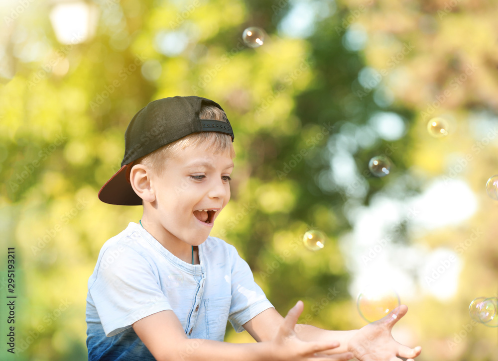 Cute little boy playing with soap bubbles in park