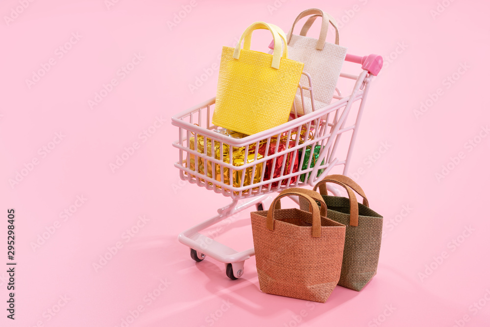 Annual sale shopping season concept - mini pink shop cart trolley full of paper bag gift isolated on