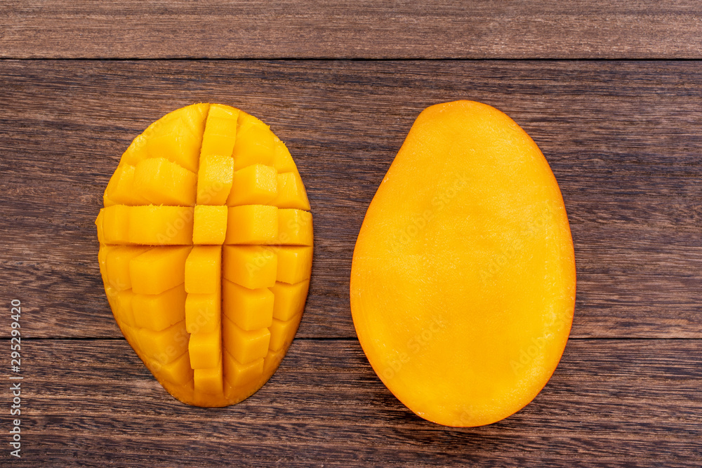 Fresh mango, beautiful chopped fruit with green leaves on dark wooden table background. Tropical fru