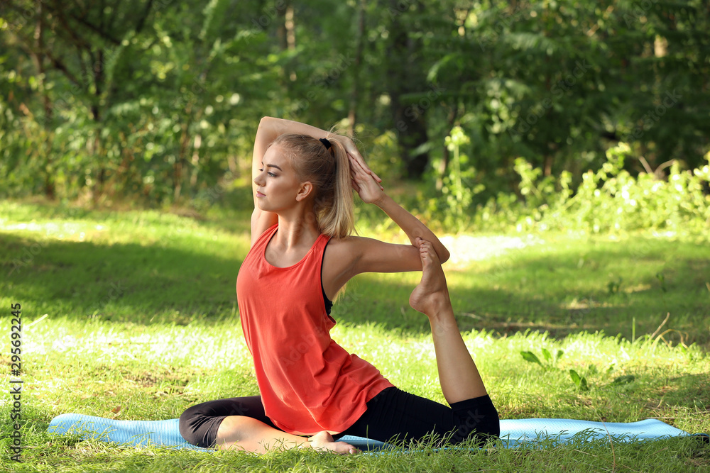 Beautiful young woman practicing yoga in park