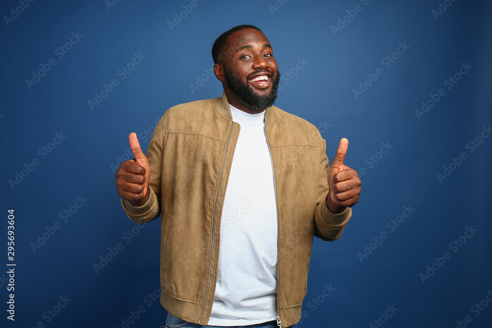 Happy African-American man showing thumb-up gesture on color background