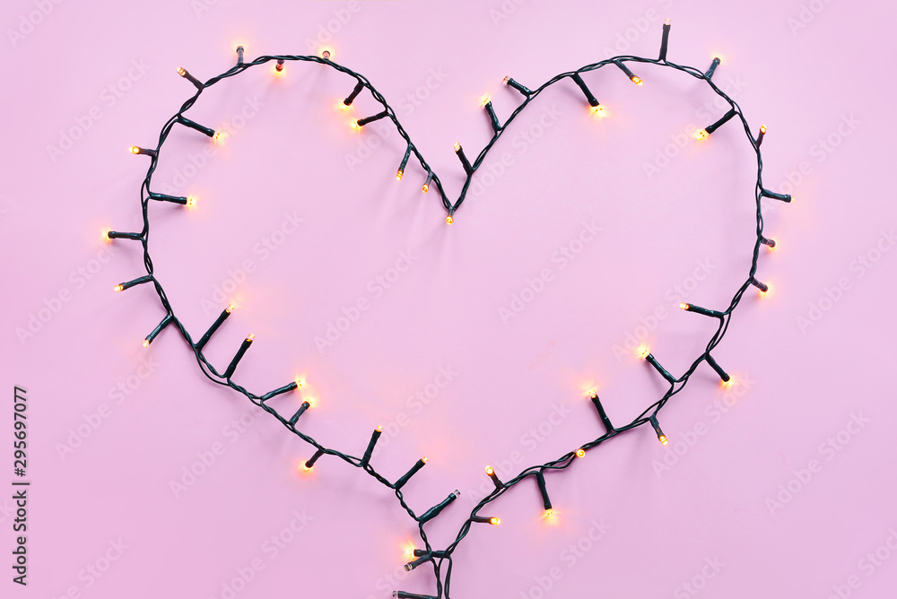 Heart made of glowing garland on color background